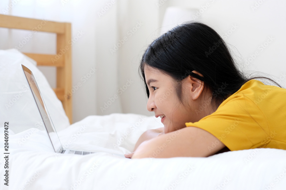Young asian woman using laptop computer while lying on bed in white room background, people and technology, lifestyles, education, business concept Young asian woman using laptop computer while lying on bed in white room background, people and technology, lifestyles, education, business concept
