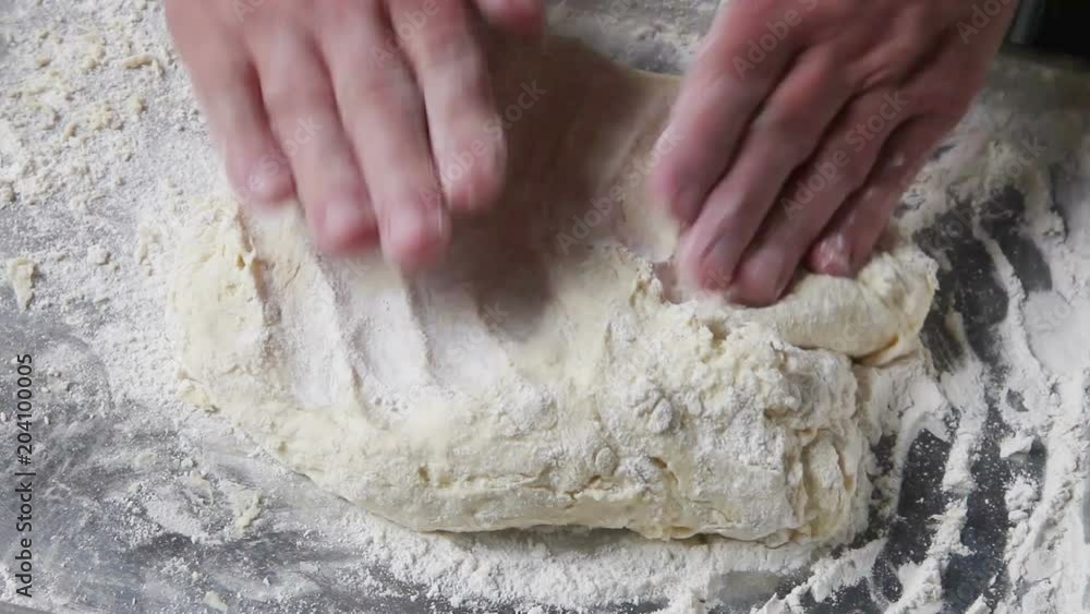 A male baker pats dough down to a uniform thickness