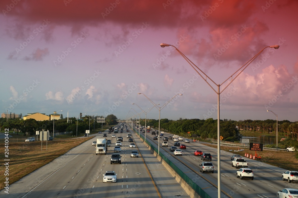 Traffic moves steadily along I-95 north and south on a hot sunny morning in rush hour under a cloudy sky accented by a red graduated filter.