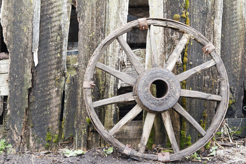 Old wooden wheel from a cart on wooden fence background. Copy space