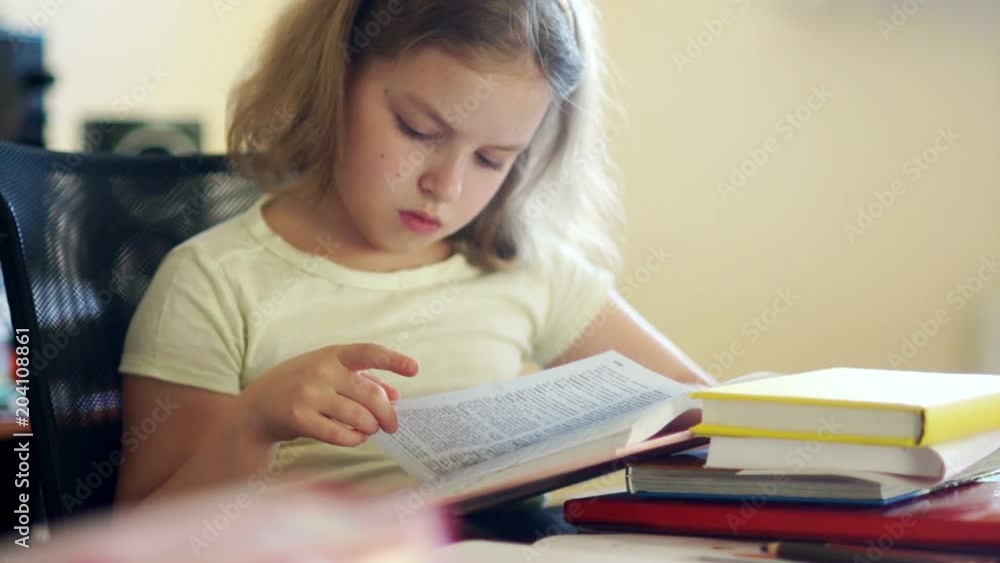 A schoolgirl reads books while sitting at a table. Home schooling. Education of children. Day of Knowledge A schoolgirl reads books while sitting at a table. Home schooling. Education of children. Day of Knowledge