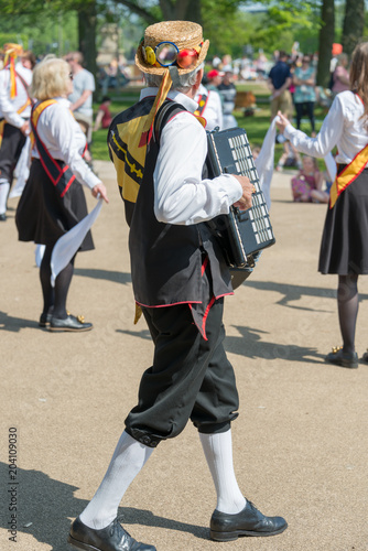 Morris dancer wearing straw hat plays accordion for the rest of the troupe on summers day in England