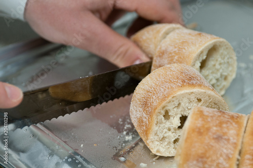 Male hands cutting baguette with bread knife for a wedding party