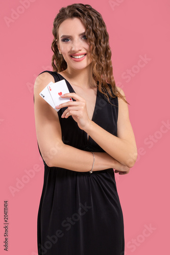 Young woman holding two aces in hand against on pink background photo