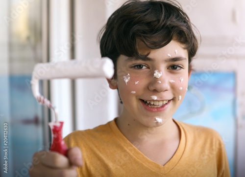 smiling teenager boy with white paint roller and dirty face make repaint close up photo photo