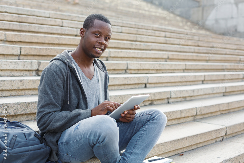 Smiling student sitting on stairs using tablet Smiling student sitting on stairs using tablet