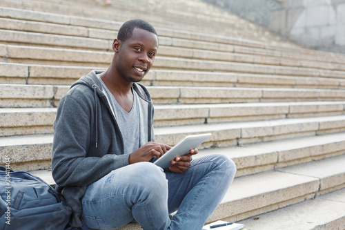 Smiling student sitting on stairs using tablet