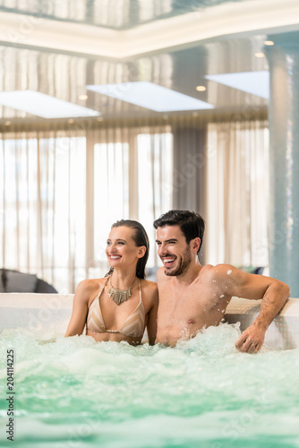 Young and happy couple in love relaxing together while sitting in jacuzzi at spa or in a luxury hotel during vacations