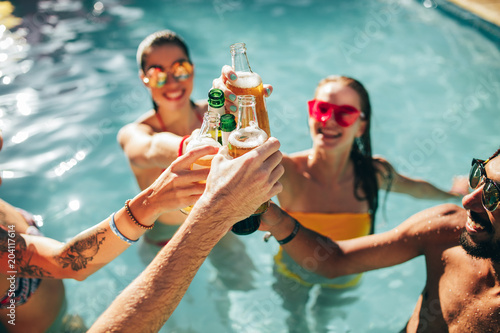 Friends enjoying and toasting drinks at pool party photo