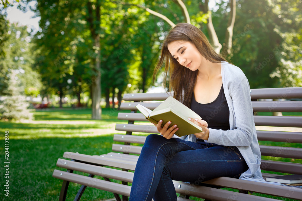 Young asian woman sitting on a bench in the park. Relaxing and reading a book Young asian woman sitting on a bench in the park. Relaxing and reading a book