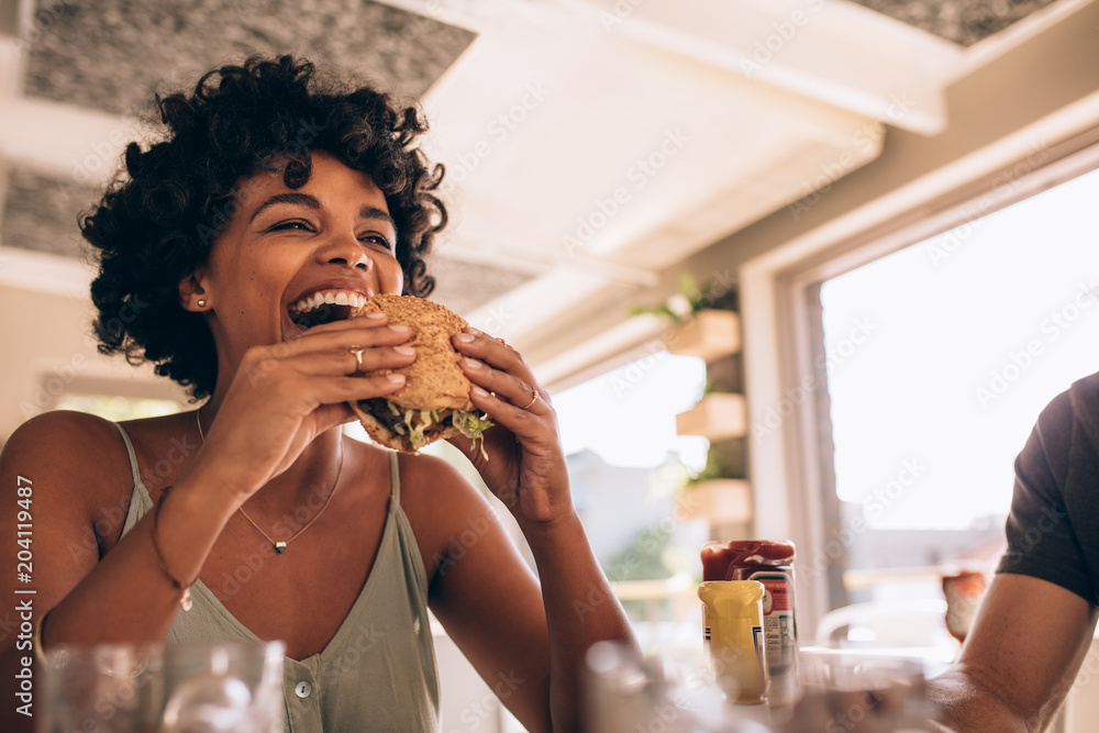 Woman enjoying eating burger at restaurant - obrazy, fototapety, plakaty 