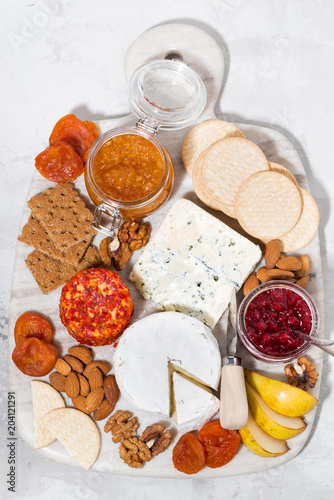 assortment of gourmet cheeses and snacks on board, top view vertical