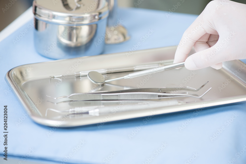 Metallic dentist tools close on and blue table sheet in a dentist clinic. with dentist hand Metallic dentist tools close on and blue table sheet in a dentist clinic. with dentist hand