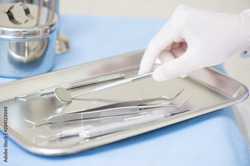 Metallic dentist tools close on and blue table sheet in a dentist clinic. with dentist hand Metallic dentist tools close on and blue table sheet in a dentist clinic. with dentist hand