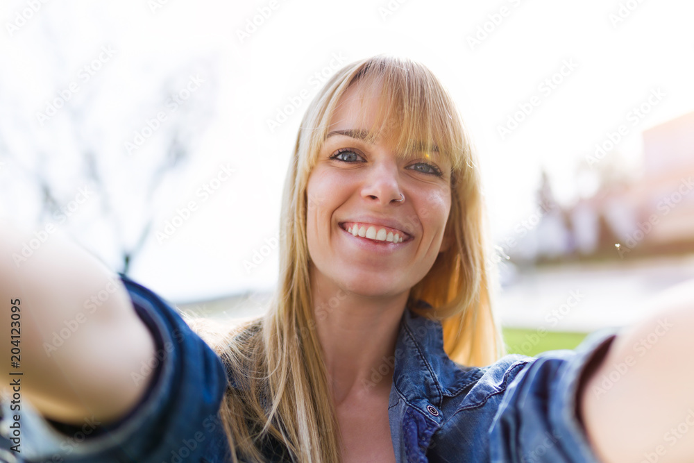 Pretty young woman taking a selfie while smiling in the park.
