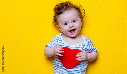 Little baby with heart shape toy on yellow background