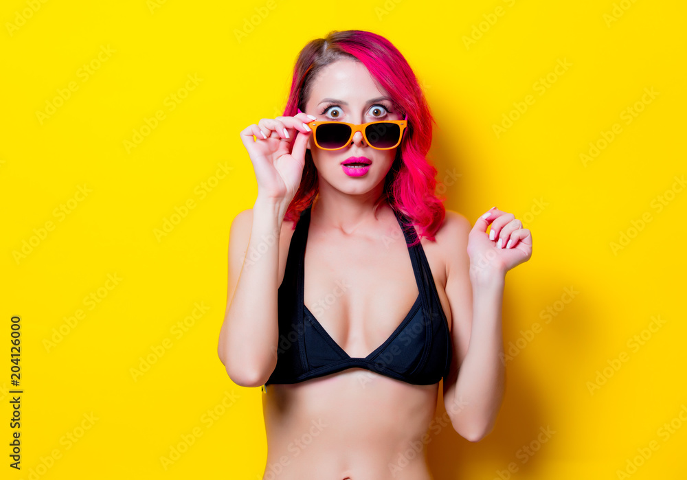Young pink hair girl in bikini and orange glasses. Portrait isolated on yellow background Young pink hair girl in bikini and orange glasses. Portrait isolated on yellow background