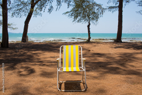 Obraz na plátně An empty yellow beach chair put by the pine tree beach showing breezy weather