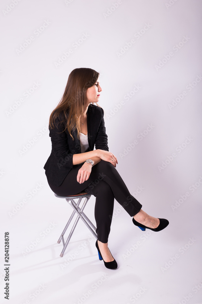 beautiful young business woman in black suit sits on a chair on white background