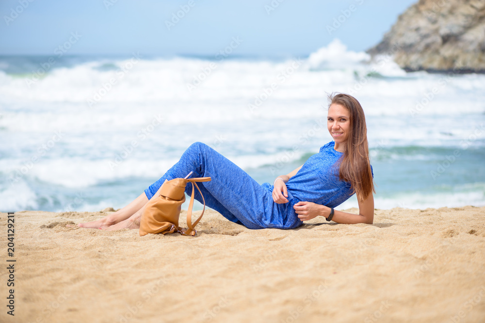 Beautiful young girl relaxing on the beach on vacation her bag nearby