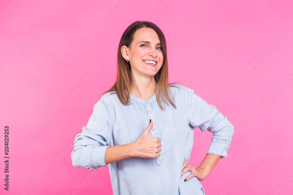 Smiling Woman in shirt posing in studio and showing thumbs up on pink background Smiling Woman in shirt posing in studio and showing thumbs up on pink background