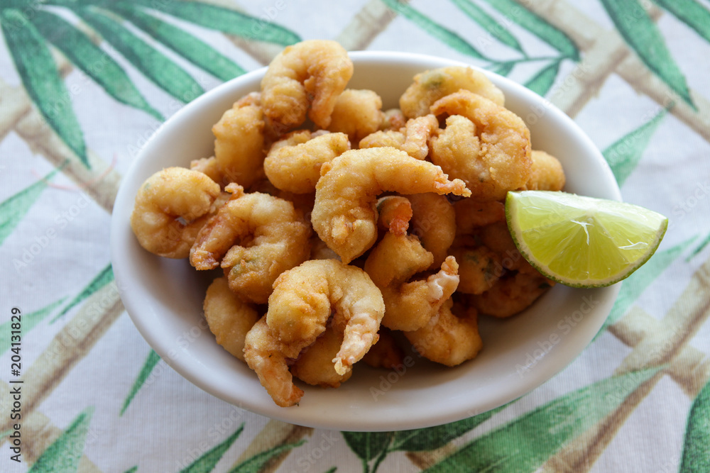 White dish of fried shrimp and lemon on table with white and green towel. White dish of fried shrimp and lemon on table with white and green towel.