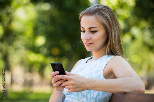 girl sitting on a bench and using phone in park