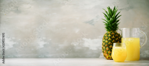 Cuadro en lienzo Pineapple juice in glassware and whole pineapple fruit on gray background