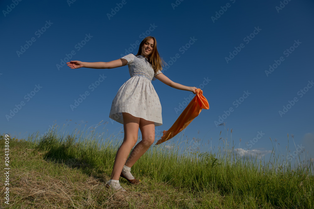 BEAUTIFUL BLONDE GIRL LAUGHS AND DANCES OUTDOORS WITH AN ORANGE SCARF IN HER HANDS BEAUTIFUL BLONDE GIRL LAUGHS AND DANCES OUTDOORS WITH AN ORANGE SCARF IN HER HANDS