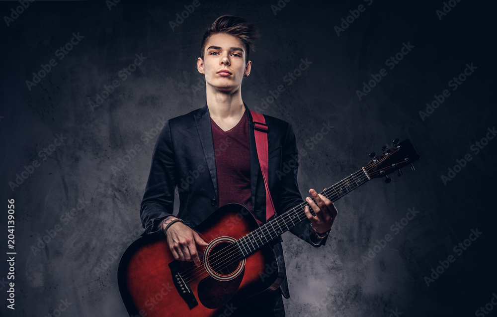 Obraz premium Stylish young musician with stylish hair in elegant clothes, playing on an acoustic guitar.