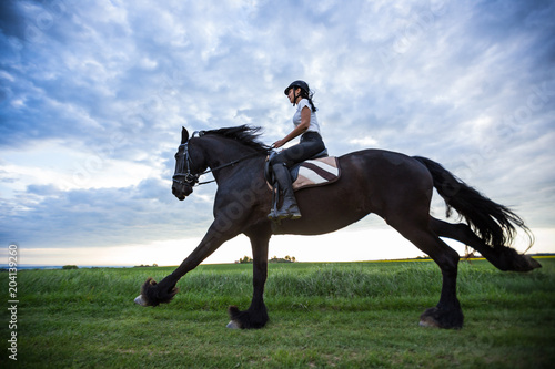 Beautiful woman riding a black friesian horse.