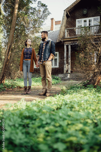a pair of hipsters in a forest near an old house