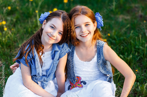 beautiful young girls in white dresses and blue flowers in teir hair in the garden with apple trees blosoming having fun at the sunset. two friends  hugging photo