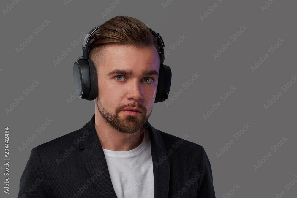 Close-up portrait of a stylish bearded man with hairstyle listening to music in headphones. Close-up portrait of a stylish bearded man with hairstyle listening to music in headphones.