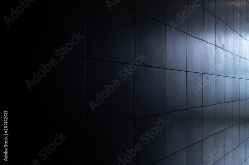 Internal wall of the room after repair, covered with gray ceramic tiles, lighting with a gradient from dark to light.