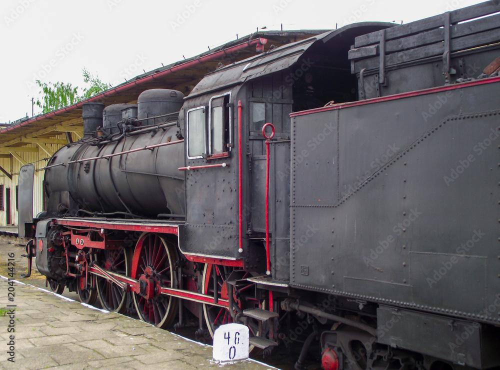 Fototapeta premium Stara, czarna lokomotywa parowa stoi na stacji, gotowa wyruszyć w ekscytującą podróż.