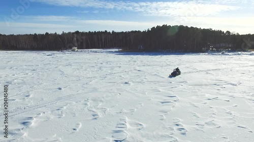 AERIAL CLOSE UP: People driving snowmobile on beautiful snowy mountain slope exploring Lapland countryside, Finland. Tourists on snowmobile adventure ride in forested winter wonderland. Snowmobiling