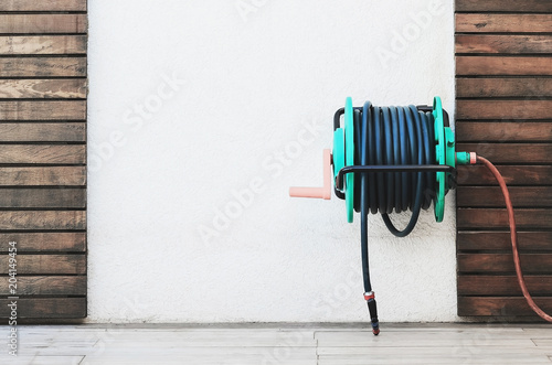 Background of a garden hose reel fixed on the wall. Blank wall on center with wooden boards decoration. photo