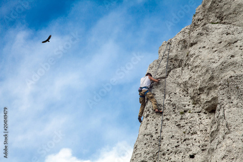 Man climbs to the top of the mountain. Rocks and blue sky. Bird in the sky and climbing wall.. To reach a top.