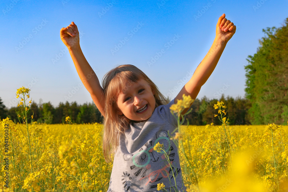 Naklejka premium The girl runs and plays on the field of flowering rape. Sunset. Portrait. Nature blooms. May. Spring.