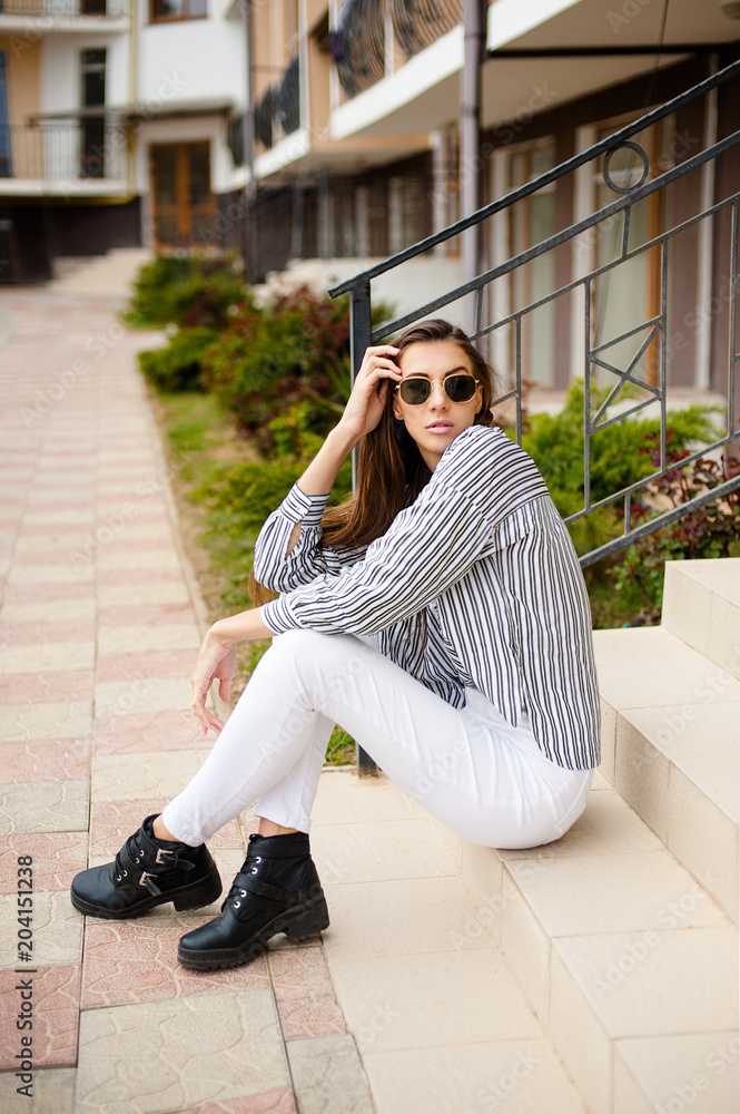 Outdoor portrait of young beautiful girl posing in street. Model wearing stylish sunglasses, stripped black-white blouse. City lifestyle, female fashion concept. Copy, empty space for text Outdoor portrait of young beautiful girl posing in street. Model wearing stylish sunglasses, stripped black-white blouse. City lifestyle, female fashion concept. Copy, empty space for text