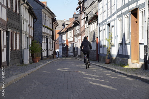 Woman driving a bicycle on a street with old nordic style houses in the town of Goslar, Germany in the Harz region.