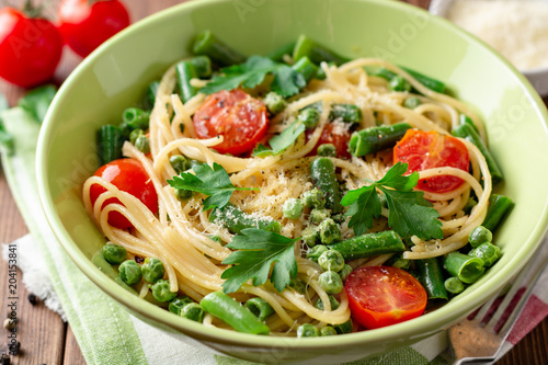 Spaghetti pasta with green beans, peas, cherry tomatoes, parsley and parmesan cheese on wooden table