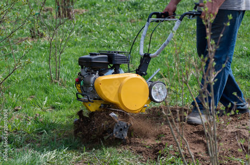 The farmer plows the land with a motoblock. The cultivator loosens the ground. photo