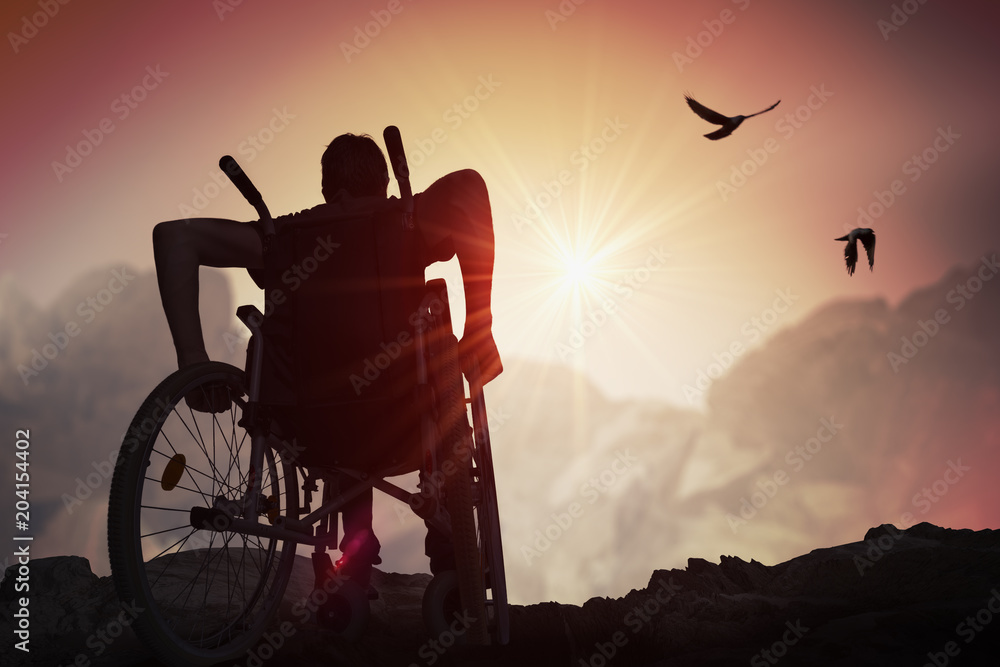 Disabled handicapped man has a hope. He is sitting on wheelchair and stretching hands at sunset. - obrazy, fototapety, plakaty 