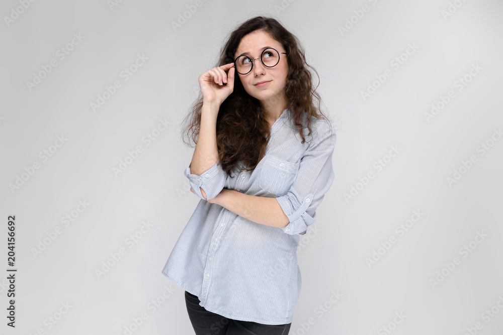 Portrait of a young girl in glasses. Beautiful young girl on a gray background. A young girl in a light blouse and dark trousers. Portrait of a young girl in glasses. Beautiful young girl on a gray background. A young girl in a light blouse and dark trousers.
