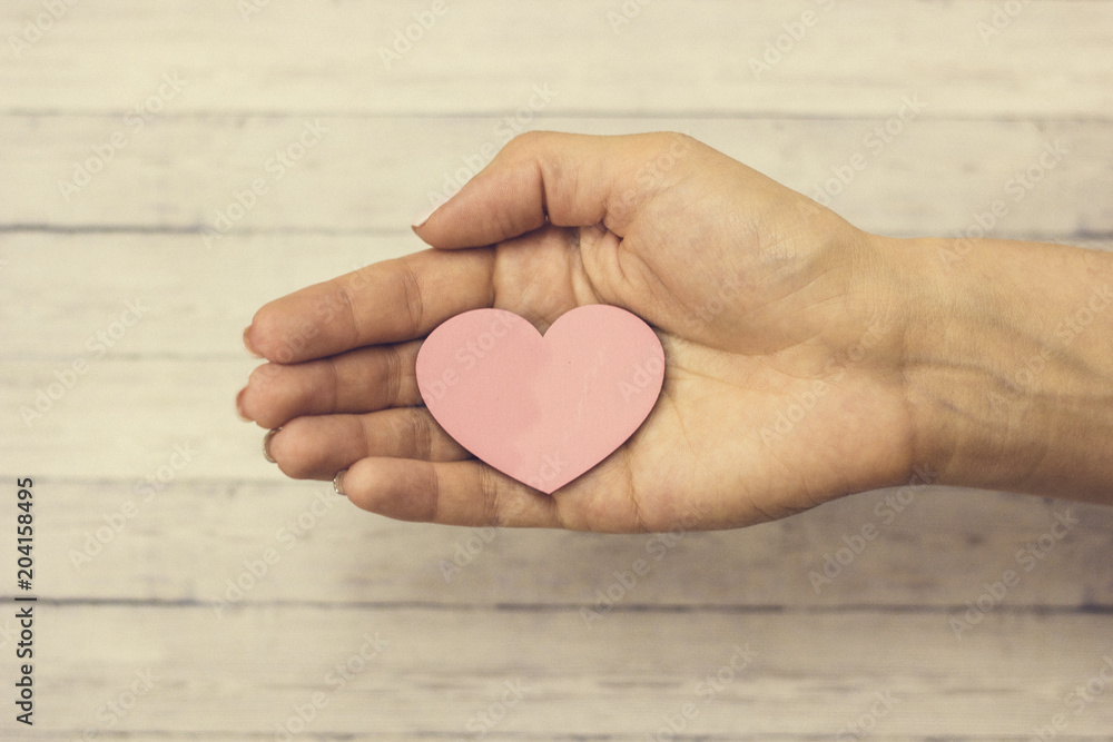A female hand holds a wooden heart, the concept of love A female hand holds a wooden heart, the concept of love