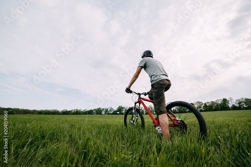 Young man riding bicycle on a meadow with high green grass. Sports, tourism and activity concept