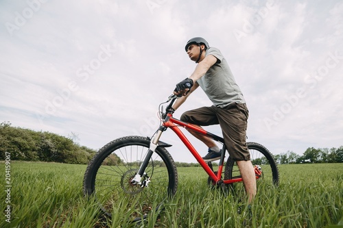 Low angle view of young man riding bicycle on a meadow with high green grass. Environmentally friendly transport, clean air, activity, healthy lifestyle concept
