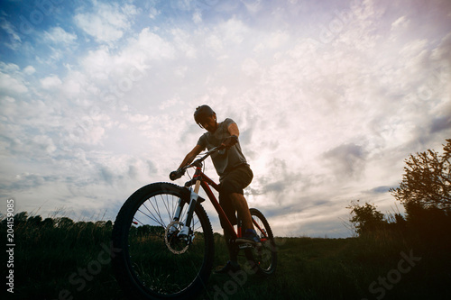 Fototapeta Naklejka Na Ścianę i Meble -  Bicycle sports, traveling, healthy lifestyle and activity. Silhouette of young man riding bicycle along a country road in sunset light